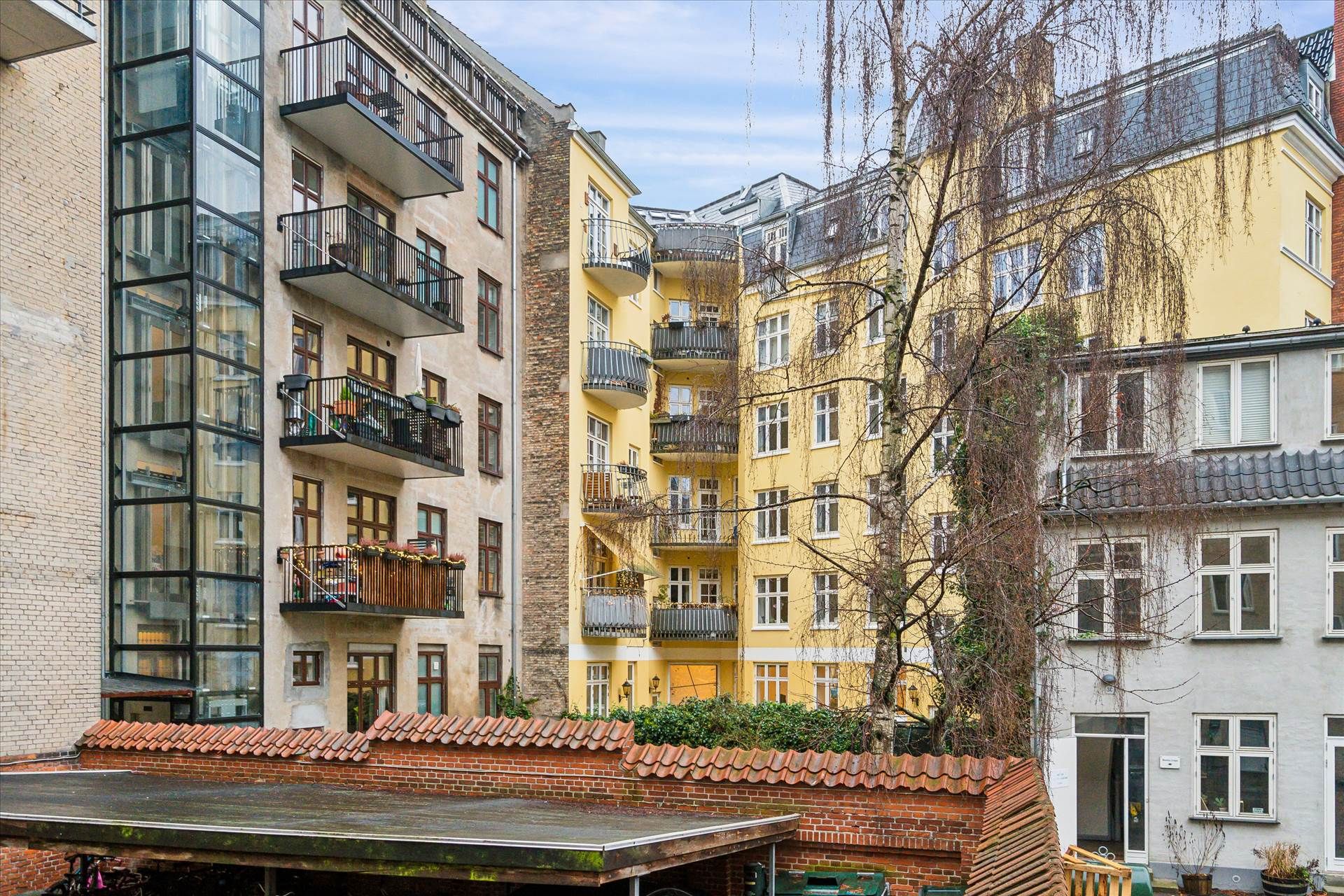 En stor gul huslejlighed med store balkoner og mange vinduer ligger i en bygning med andre huslejligheder og store ruder