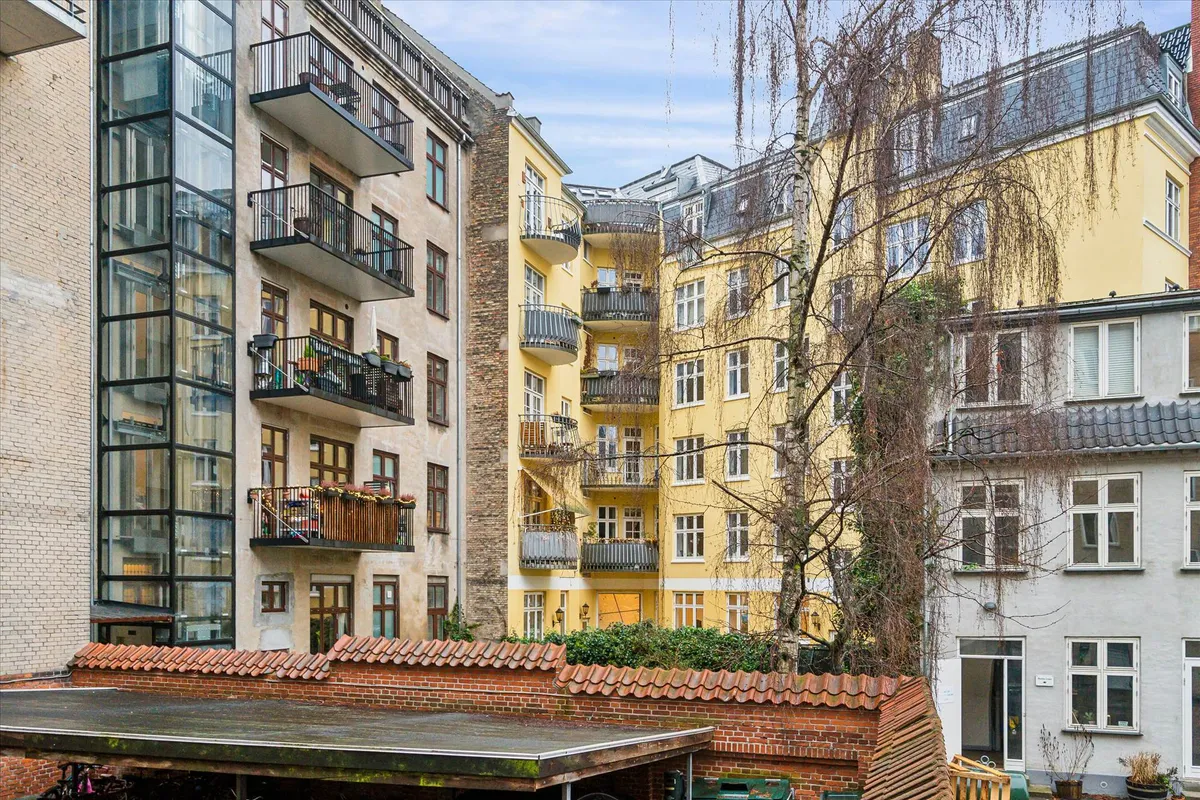 En stor gul huslejlighed med store balkoner og mange vinduer ligger i en bygning med andre huslejligheder og store ruder