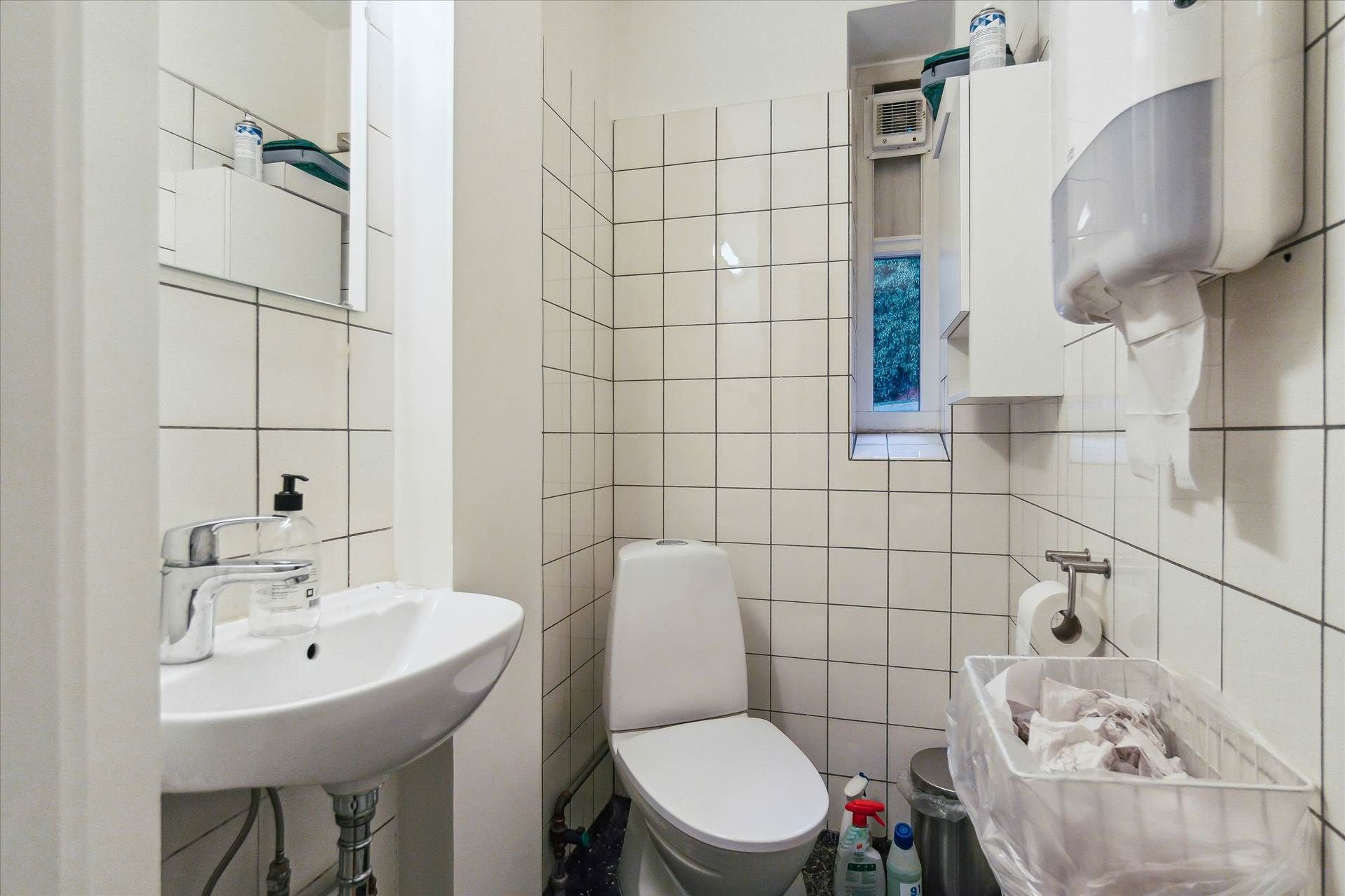 Toilet med hvidt toilet, hvidt vasketøjsskab, hvid vask og håndklædeholder samt håndklæde, håndsæbe og luftfrisker i en