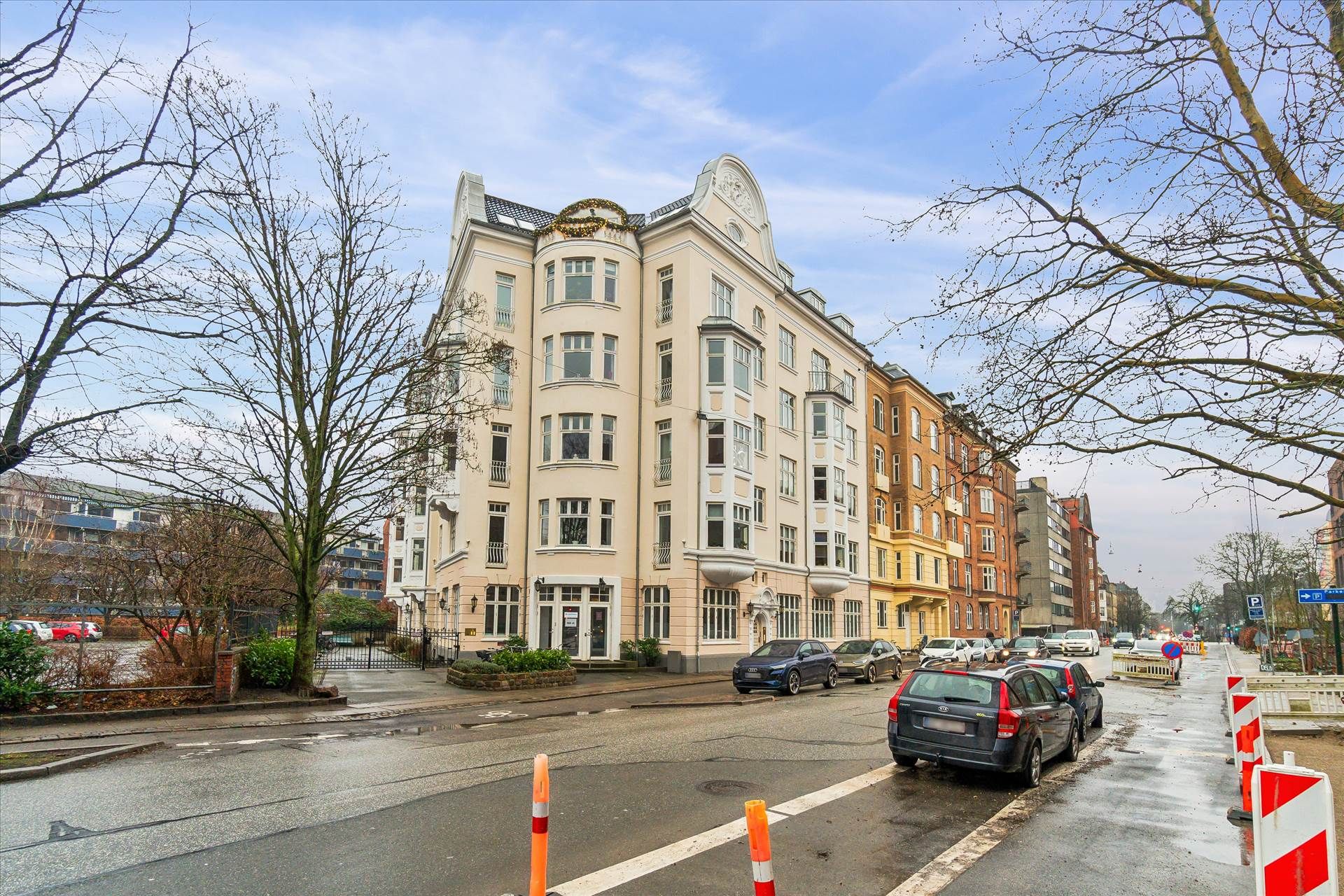 Hjørnebygning med hvidpuds og store vinduer, liggende i en bygning med flere køretøjer parkeret langs vejen og