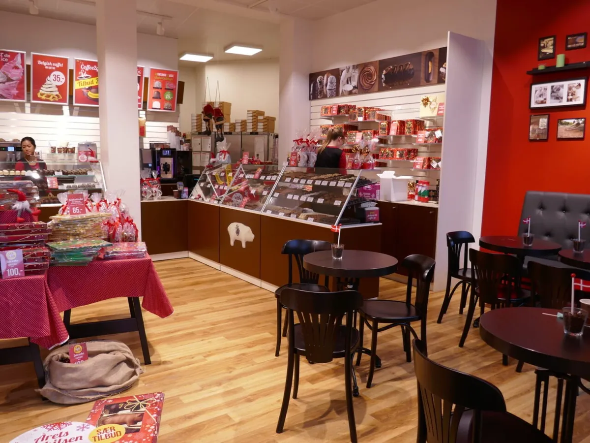 En konfektbutik med flere kunder og personale, der står ved sælgerne og sælger chokolade og andre konfekter