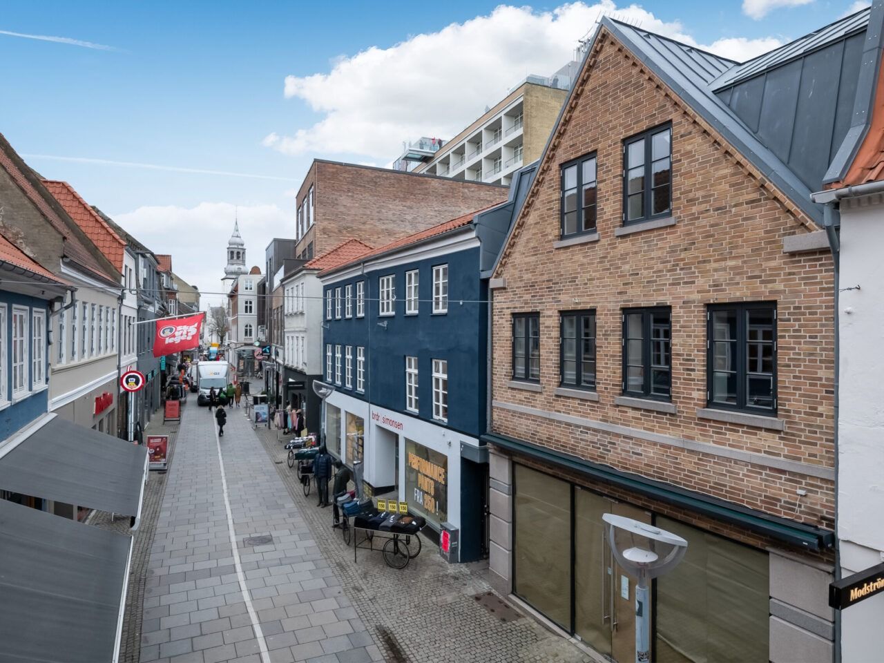 Gågade med forretninger og gående folk samt et rødt banner med en sort tekst i Aalborg