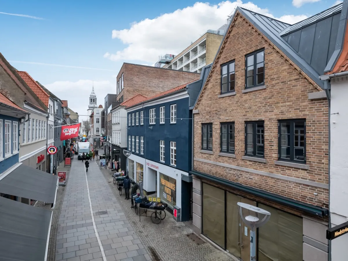 Gågade med forretninger og gående folk samt et rødt banner med en sort tekst i Aalborg