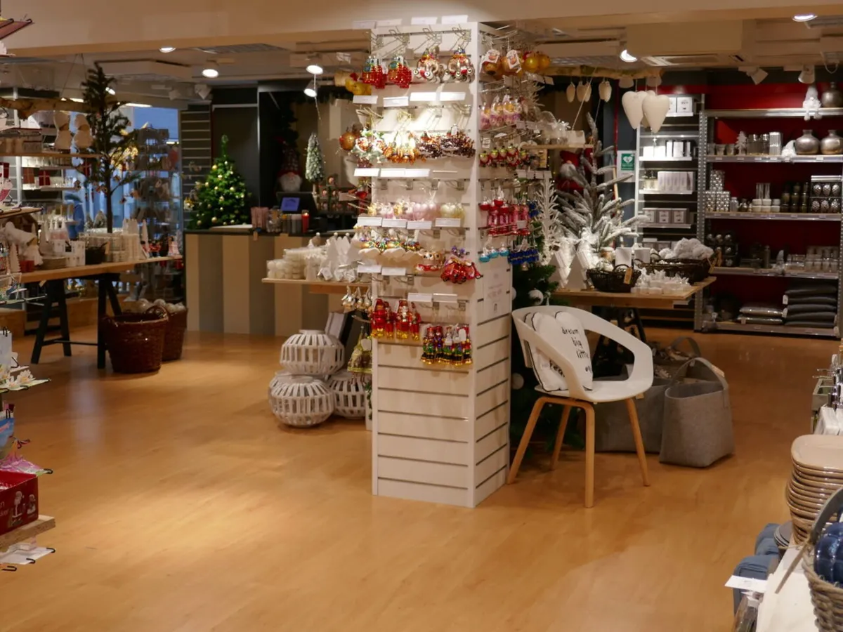 Indvendørs i en indkøbsforretning med trægulv, hvor der er stole, kurve og hylder med ornamenter og produkter