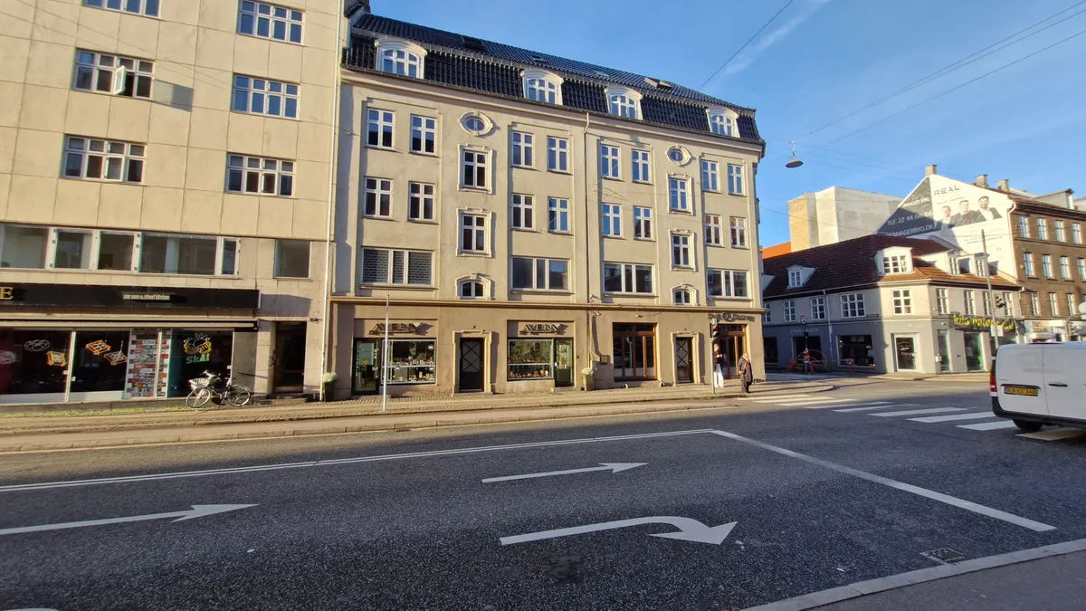 En tom gade med enkelte bygninger og butikker. På hjørnet er der en bygning med skiltet "Skål" og en cykel parkeret.