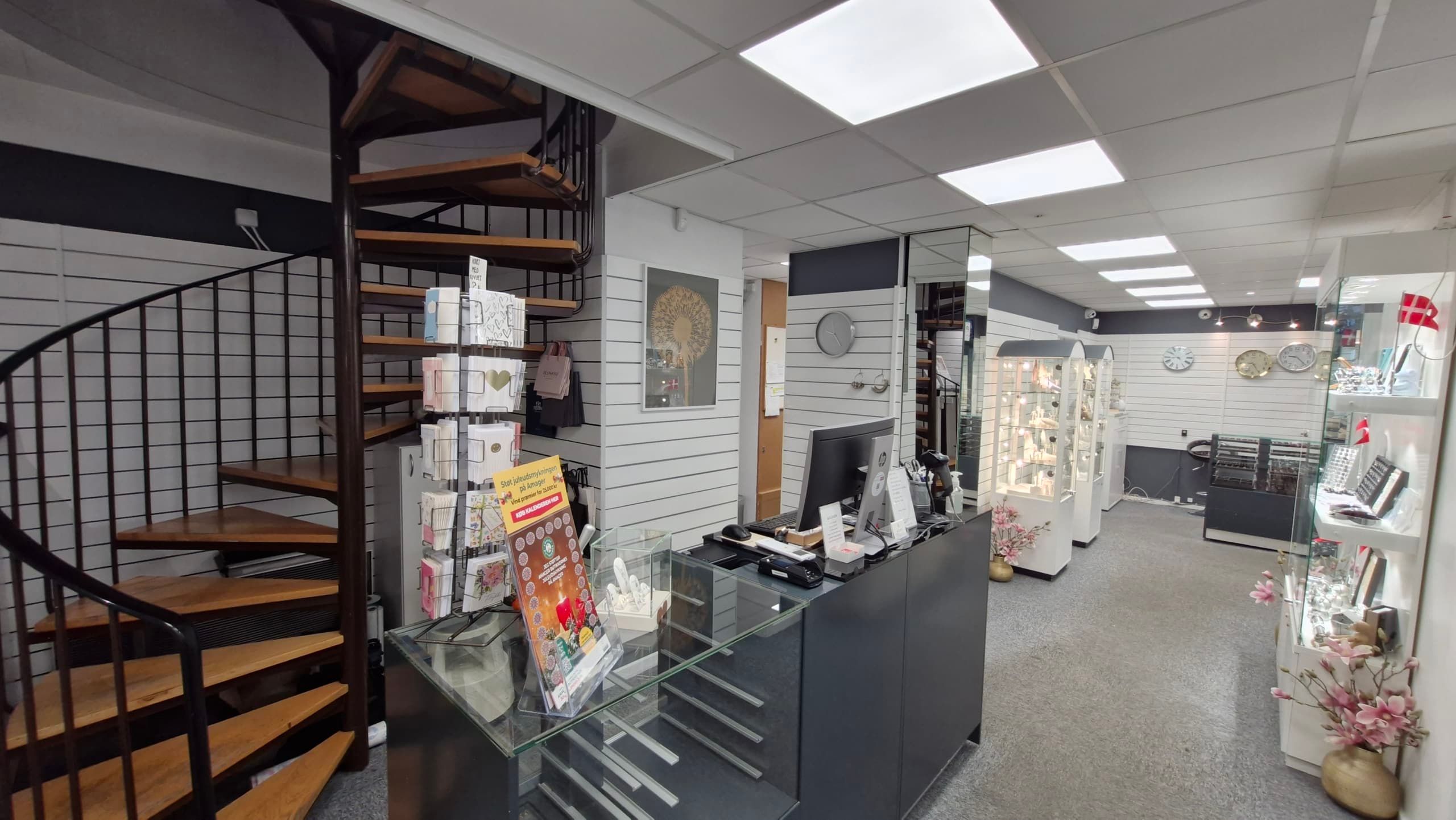 En moderne indretning med et stort glasbord, lyse loftsbelægninger, en spiraltrappe og et elegant salgsregnskabssystem.