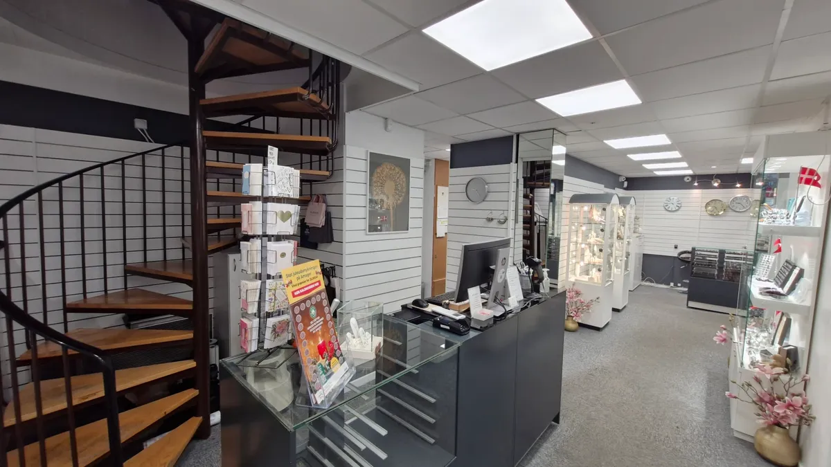 En moderne indretning med et stort glasbord, lyse loftsbelægninger, en spiraltrappe og et elegant salgsregnskabssystem.