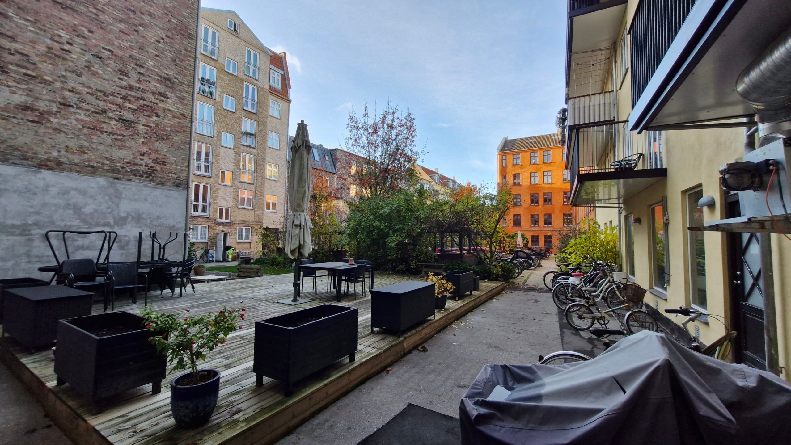 Forside med bord og stole og paraply samt potteplanter og cykler i kø