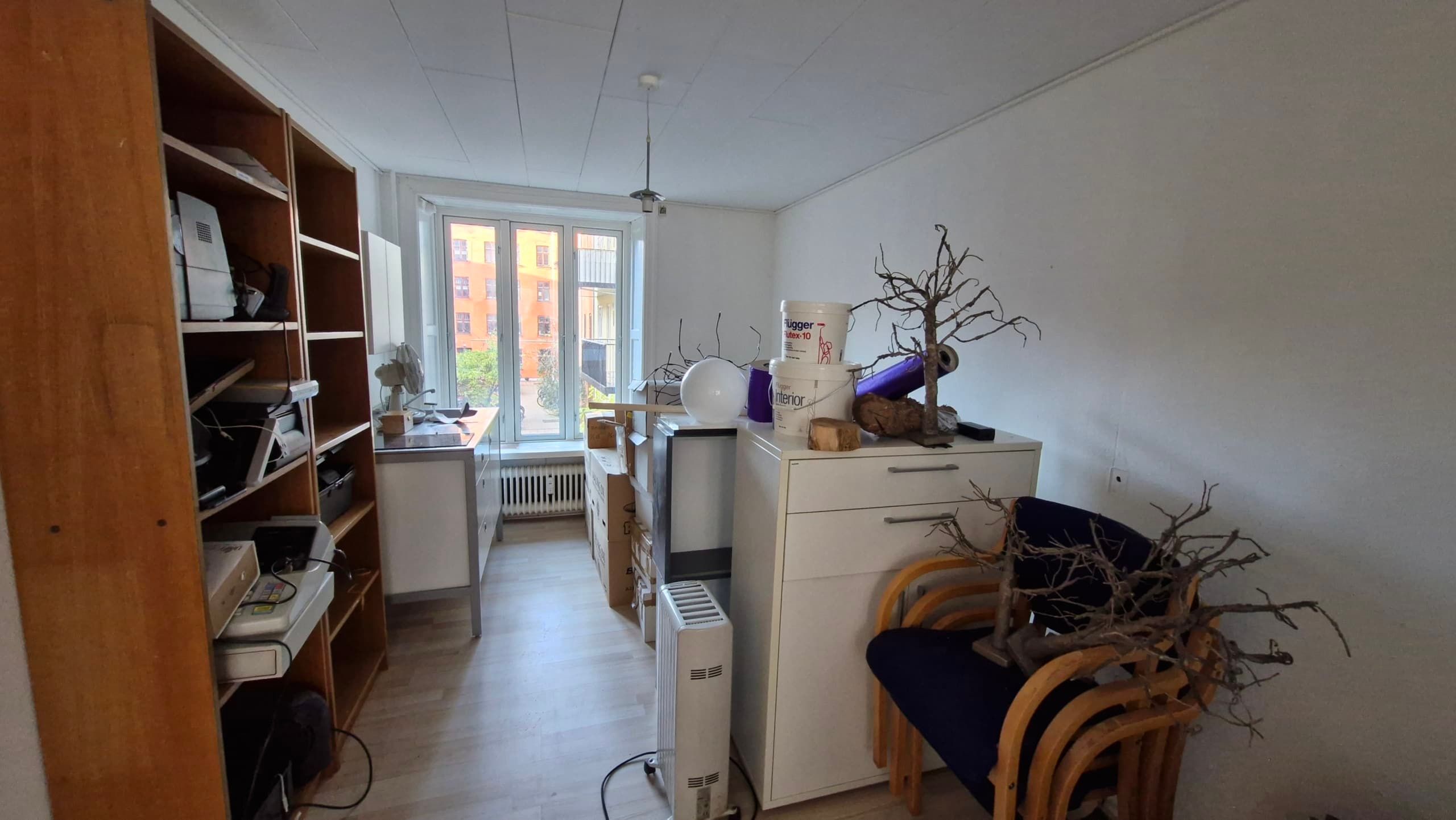 Studieværelse med højt, træhylde, skrivebord, bokse, apparater, træstole, hængende lampe, gardiner og bygningsudsigter