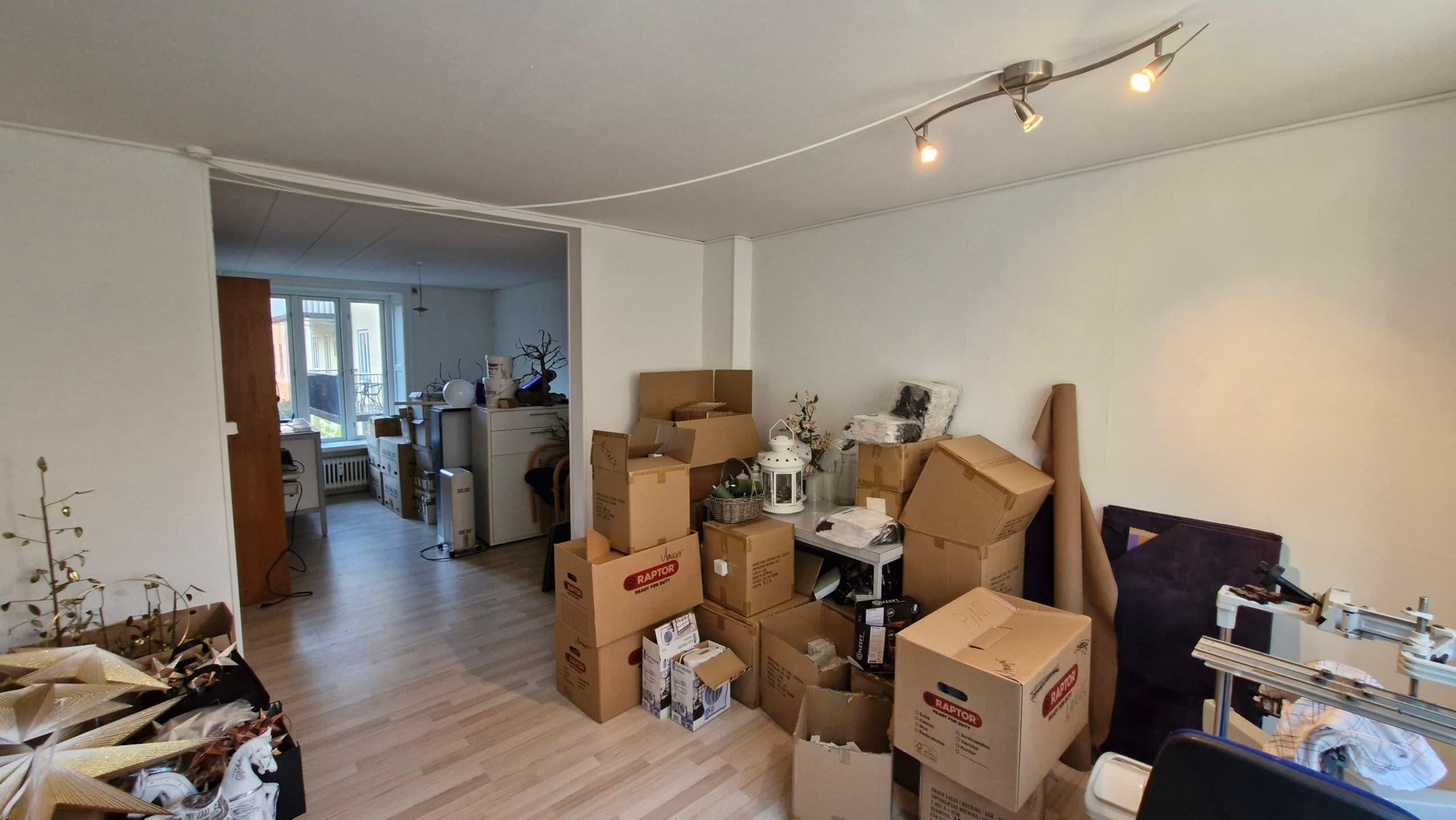 Mange bokse med diverse indhold, herunder træfigurer og blomster i en hvidrummet og lyst lokale med trægulv og hvide vægge