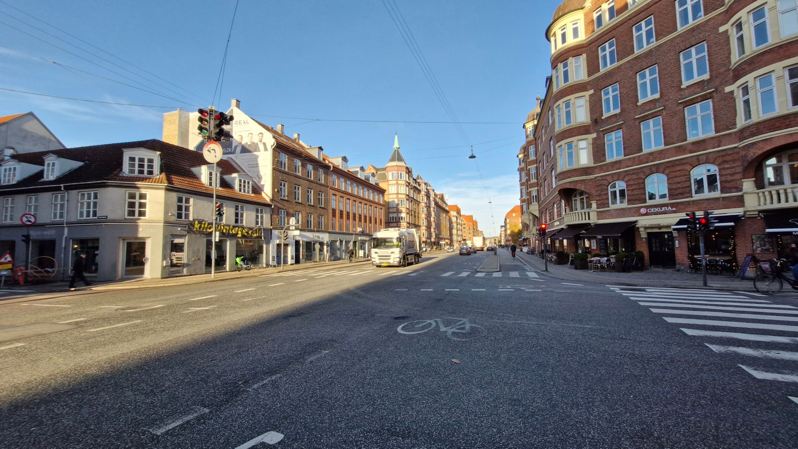 Tom gadeparti på Amagerbrogade med gågade, cykelparkering og forretninger, samt trafiklys og biler på vejen