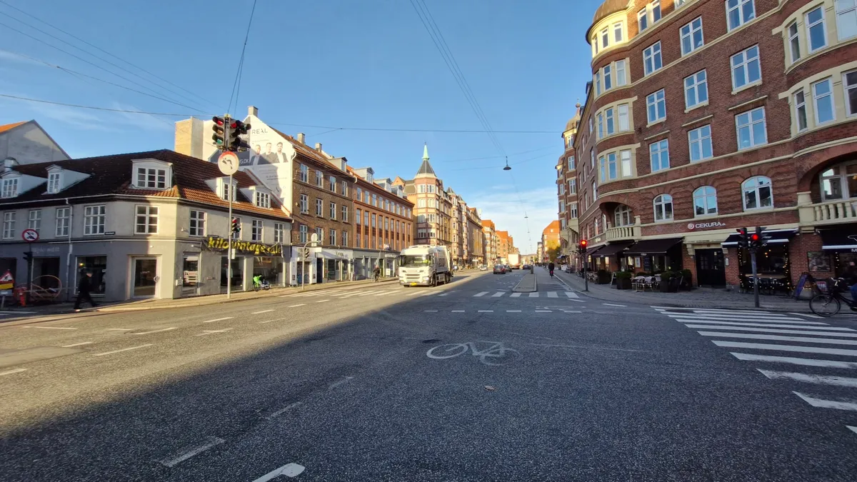 Tom gadeparti på Amagerbrogade med gågade, cykelparkering og forretninger, samt trafiklys og biler på vejen