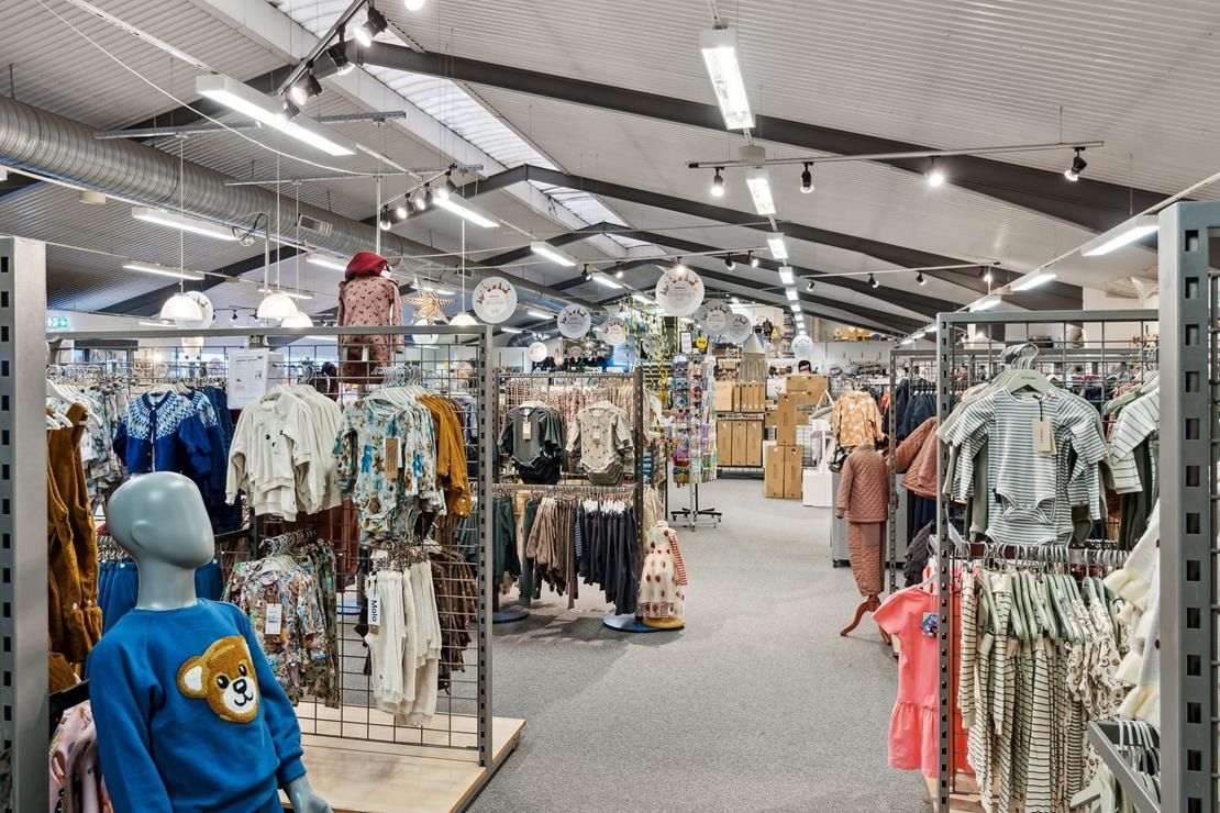 En stor butik med mange tøjreoler og tøj i farverigt sortiment, der henger i rækker på høje stativer