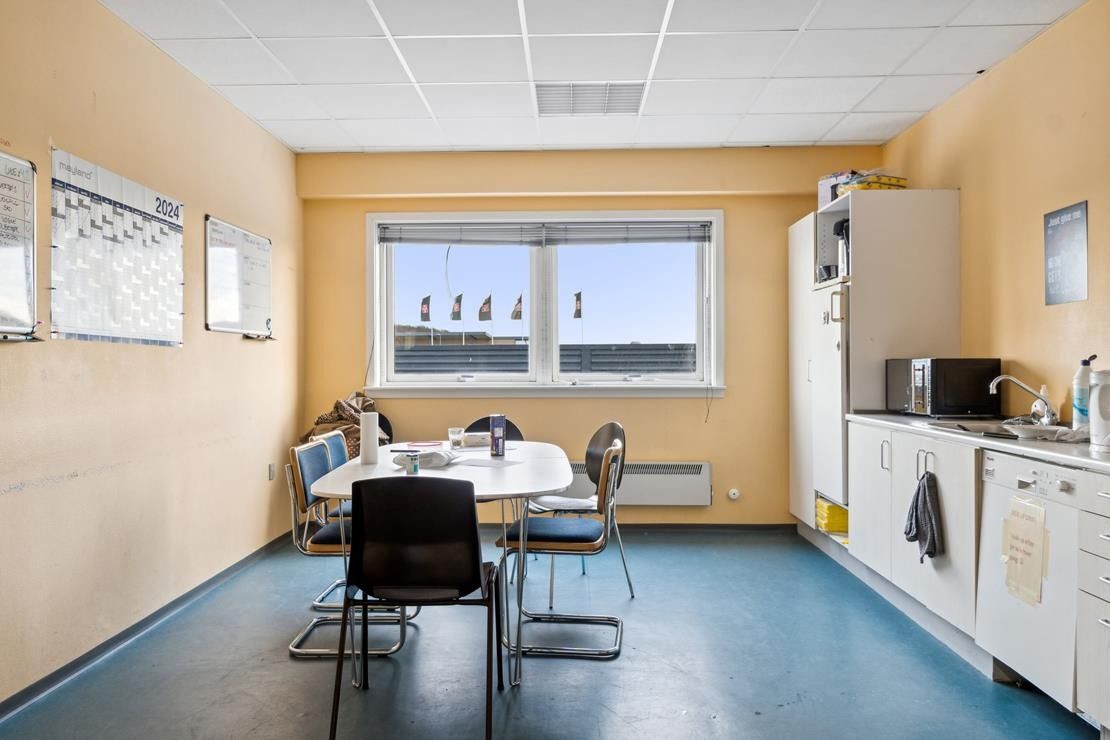 En enkelt kontorlokal med lysegul væg og gul gulv, en stor vinduesparti med udsigt, et rundt spisebord og stole samt en hvid