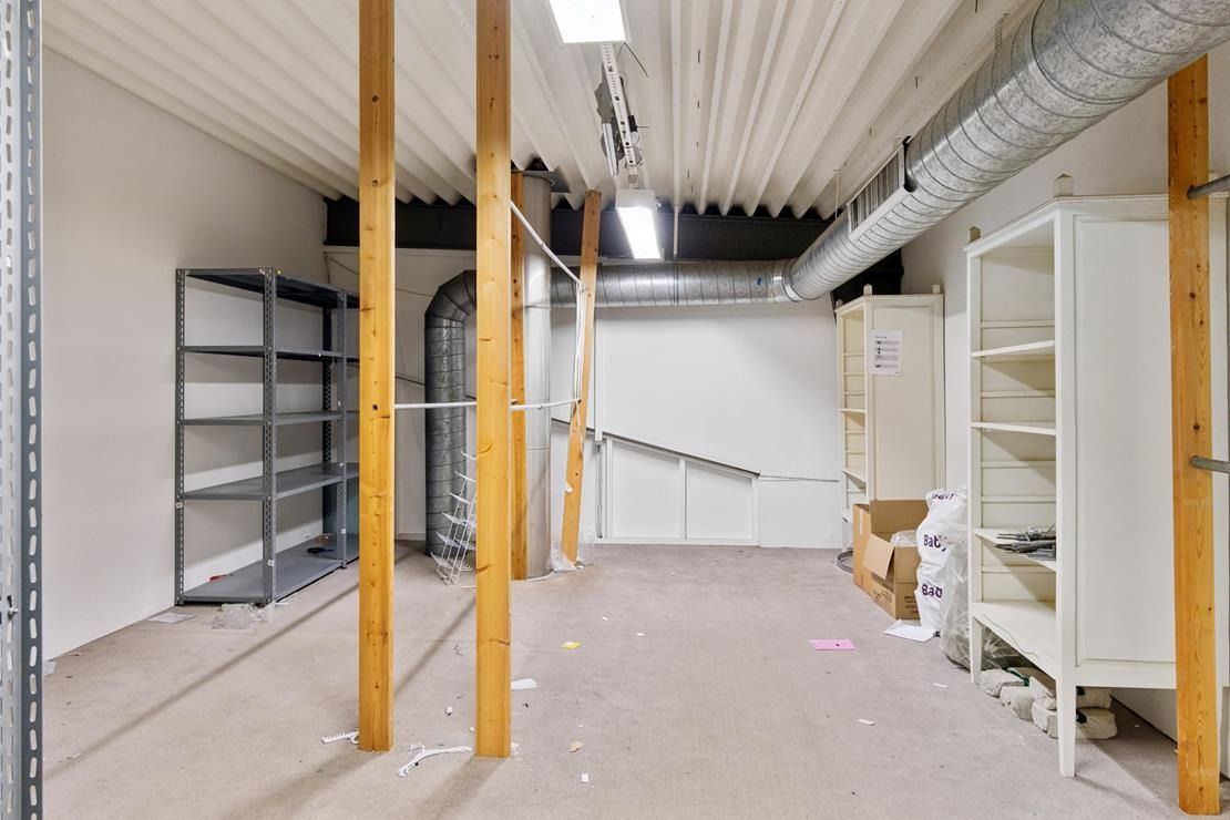 En stor forretningslokal med loftsbjælker og vægge, hvor der er to høje hylder og en høj stel på højre side.