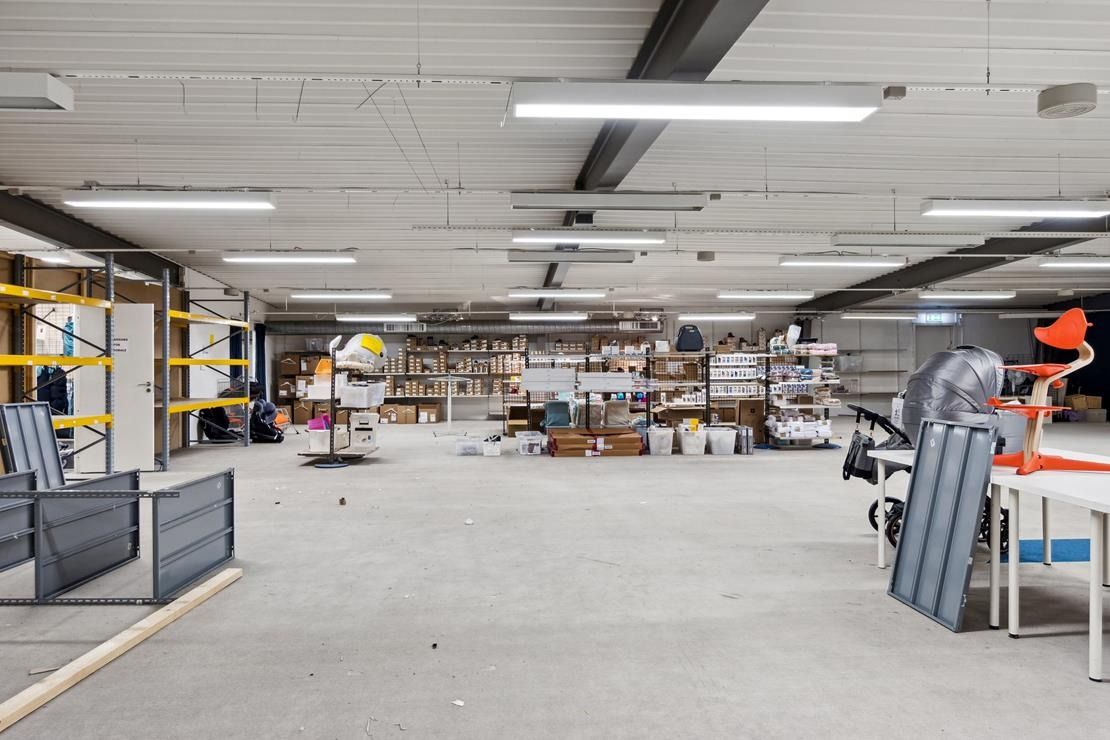 En stor butikslokal med mange hylder, bøsser og lagervogne samt moderne lys.