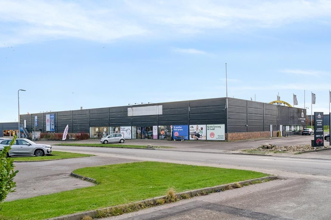 En stor bygning med mange reklamebanner, parkeringsplads og vej, og biler parkeret foran