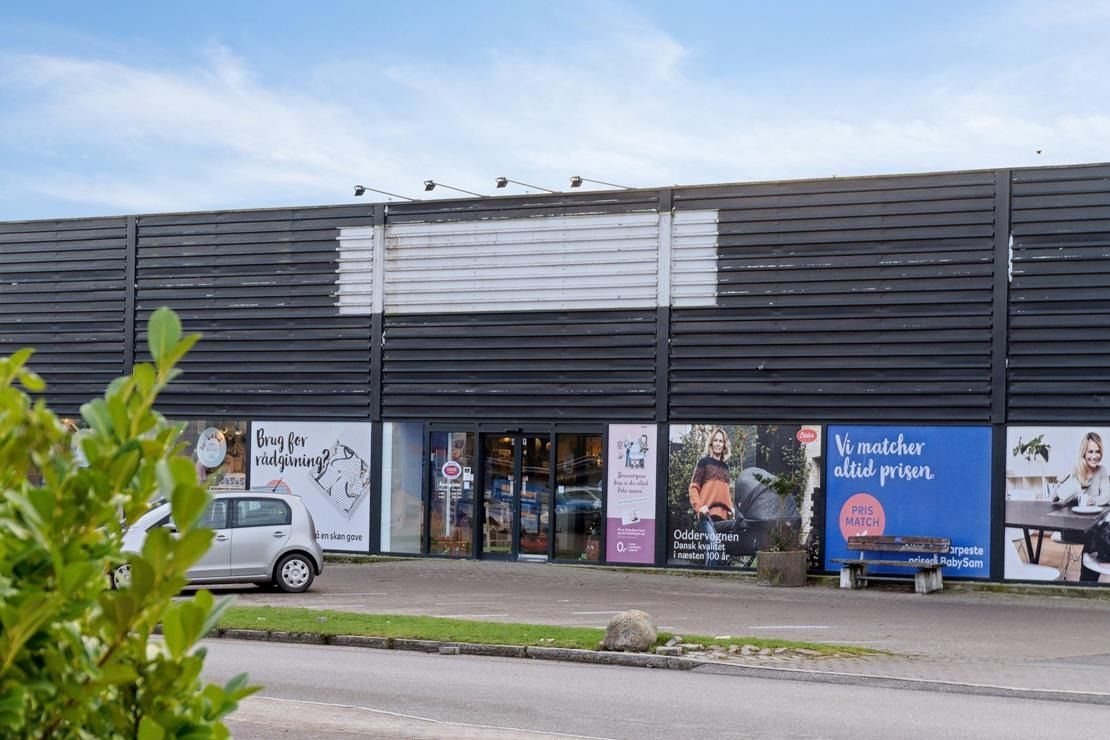 En bilparkeret ved siden af et butikslokale med skilte med tekst og billeder af børn og voksne