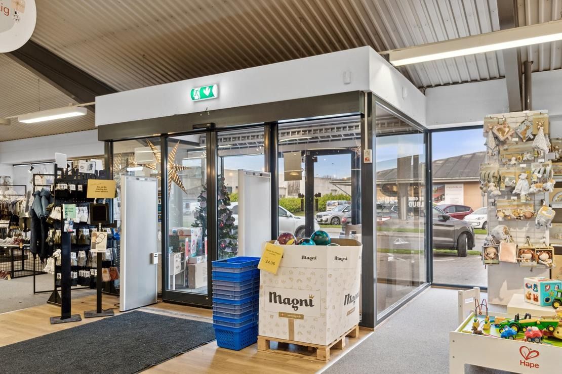 Butik med forskellige varer og stol med legemærker samt åben dør og udendørs parkeringsplads med biler