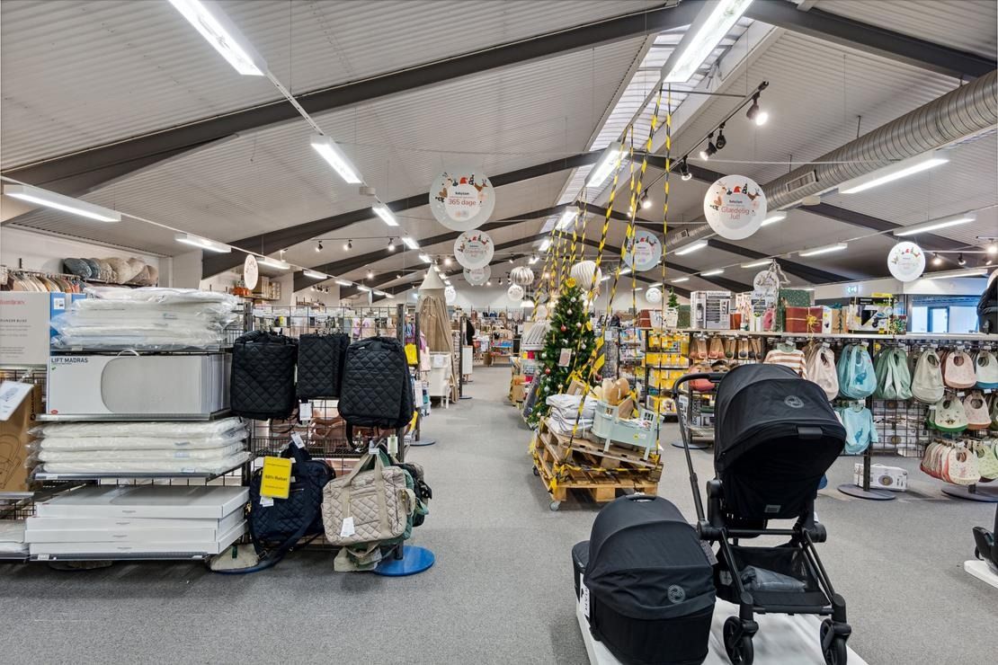 Moderne butik med udvalg af babyprodukter, herunder krybbemadrasser, tasker og klapvogne, under en hvid loftskonstruktion.