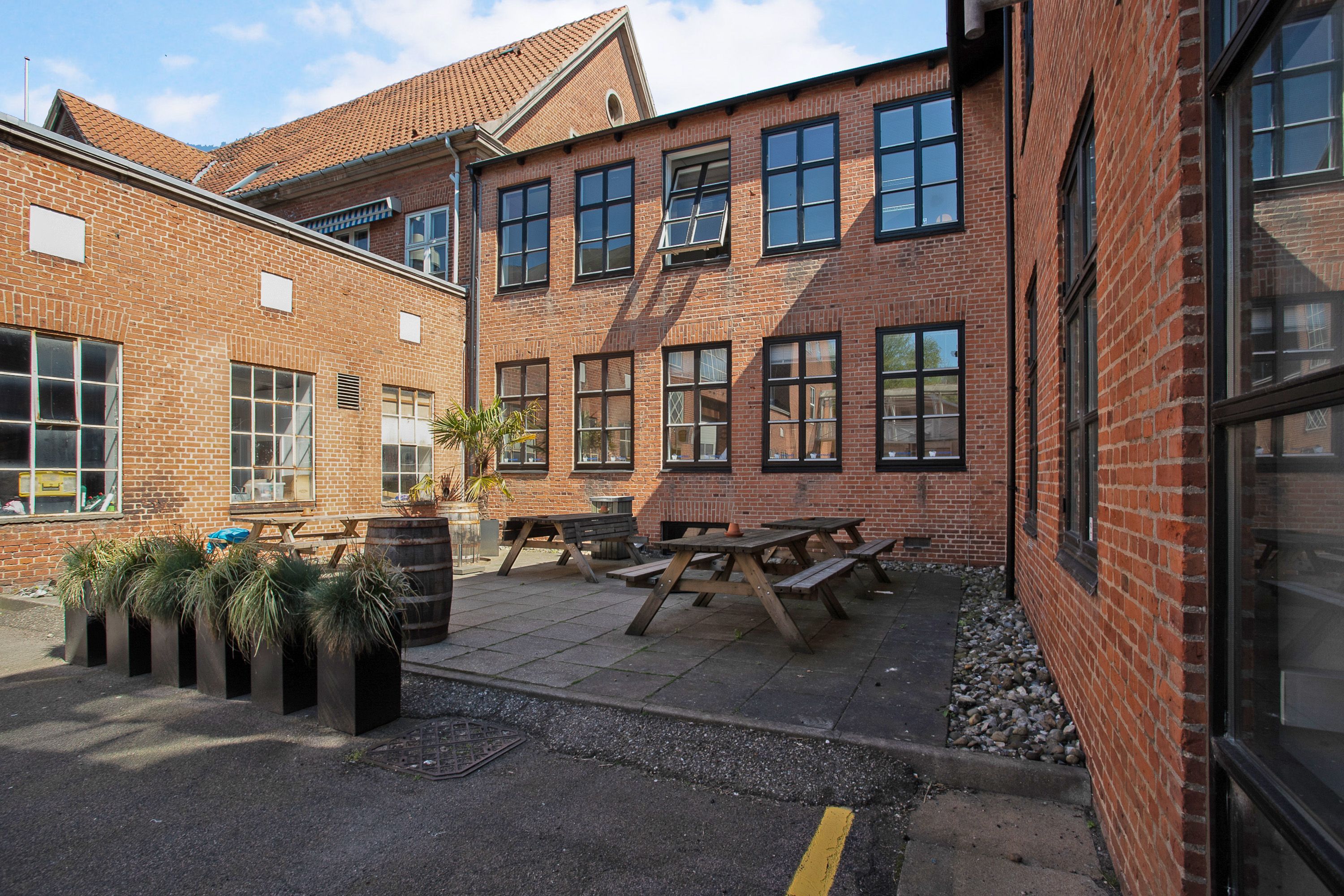 Terrasse med picnicborde og bænke i en køkkenhave omgivet af røde mursten og glasvinduer