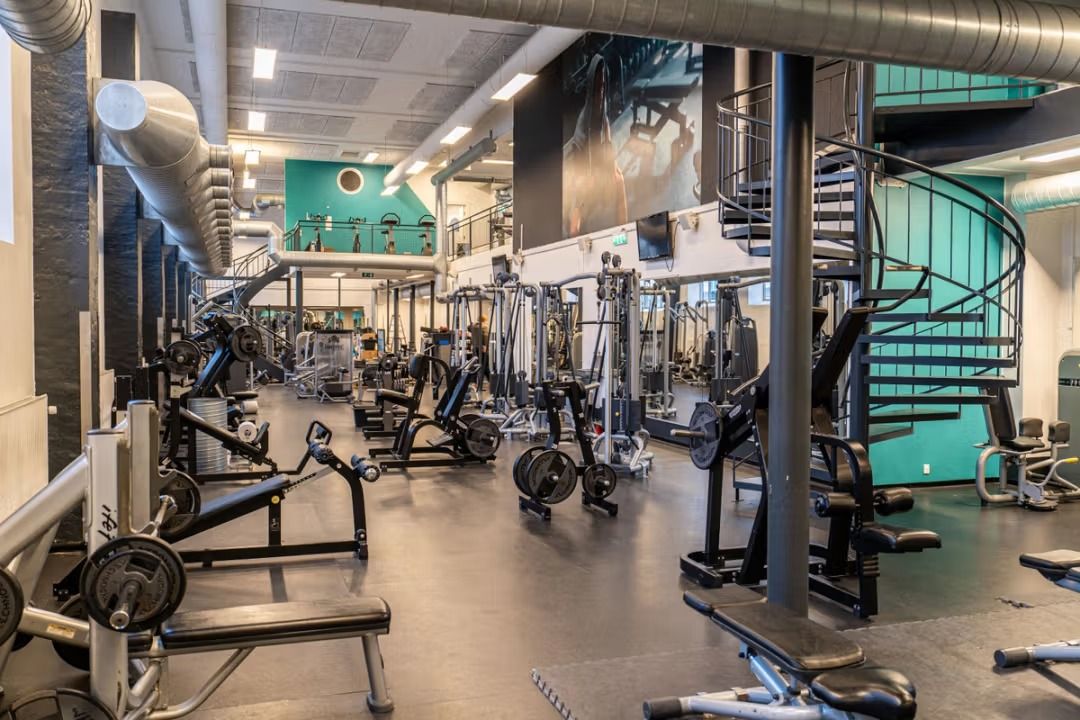 Et stort fitnesscenter med mange fitnessapparater og træningstræningsmaskiner fordelt i lokalet med et stort billede på