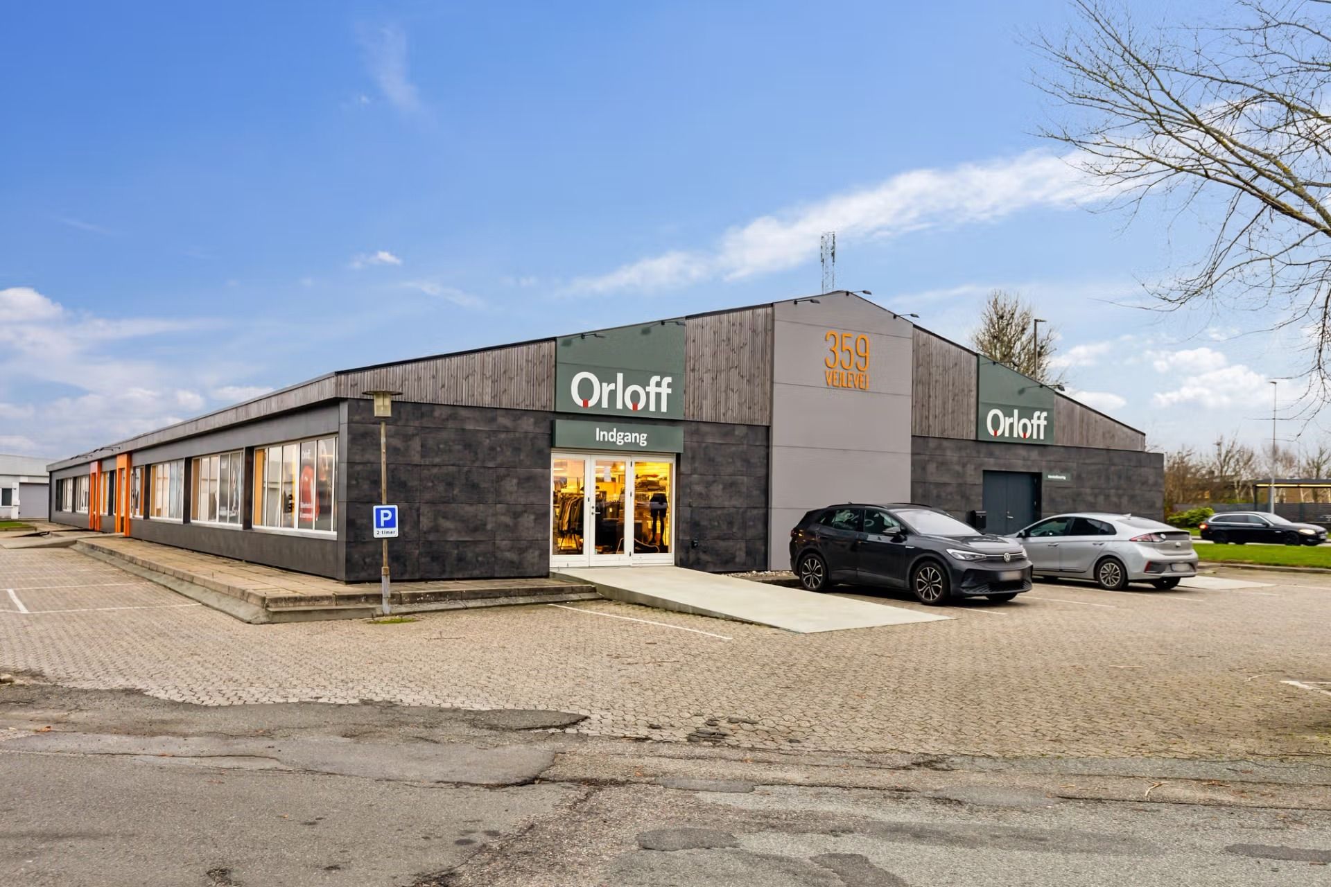 Orloff butikslokal med 359 m2 salgsområde, hvor to biler er parkeret foran og et parkeringsskilt er opstillet til venstre