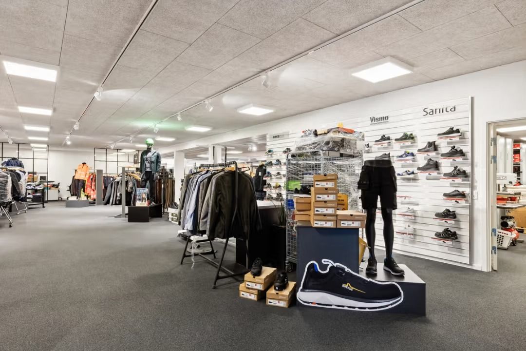 Butik med sko, tøj og sportudstyret. Sorte og hvide sko står fremtrædende. Et tøjhygge er ophængt på væggen.