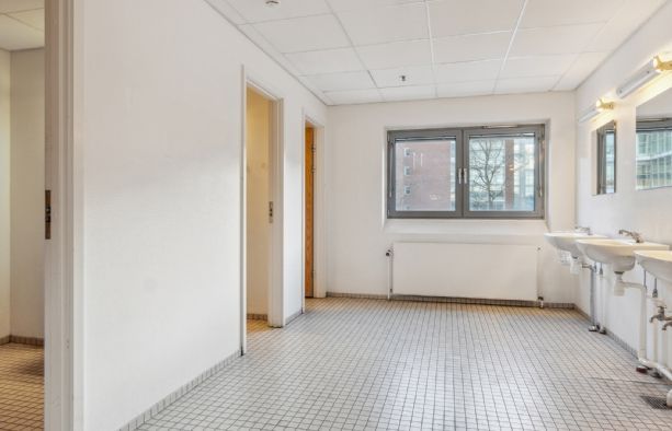 To toiletter med hvide vægge og gulve samt hvide bænke og spejle med lysekroner i en nøgen stue