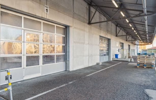 Lager med stor garagedør og nummer 1 på siden, tømmerpakker og metalbøjler på siden og en høj lysbelyst tagkonstruktion