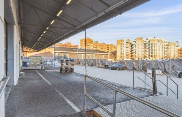 Lager med udsigt til bygninger, lastbiler og biler i baggrunden, metalliske håndværk, trin og stiger.