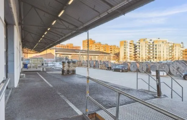 Lager med udsigt til bygninger, lastbiler og biler i baggrunden, metalliske håndværk, trin og stiger.