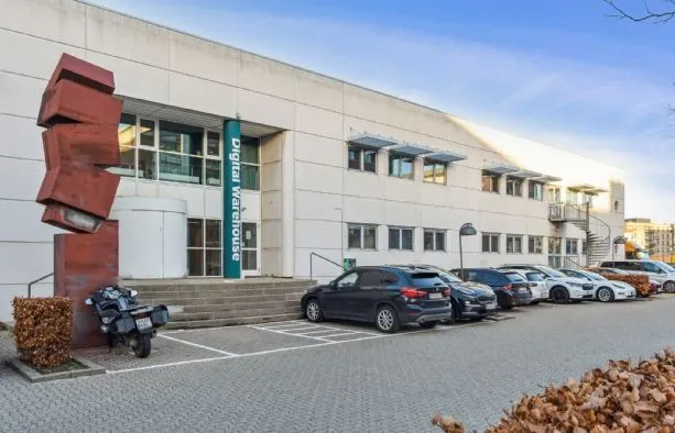 Digital Warehouse er placeret i en bygning med flere biler parkeret. Foran er der et rødt kunstværk.