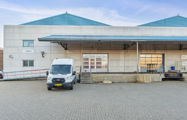 En stor last mile lagerbygning med blå tag og hvide vægge parkeret foran en hvid Ford Transit-varevogn