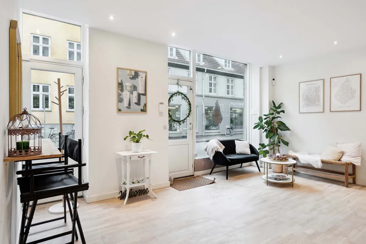 Moderne stue med hvide vægge, lyse trægulve og minimalistisk møbleret med sofa, høj bord og store vinduer