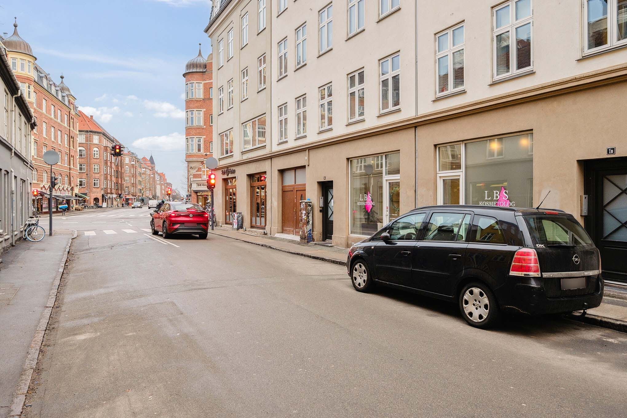 En bil kører gennem gaden, og en anden bil står parkeret ved siden af en bygning med et kosmetologisk vindue
