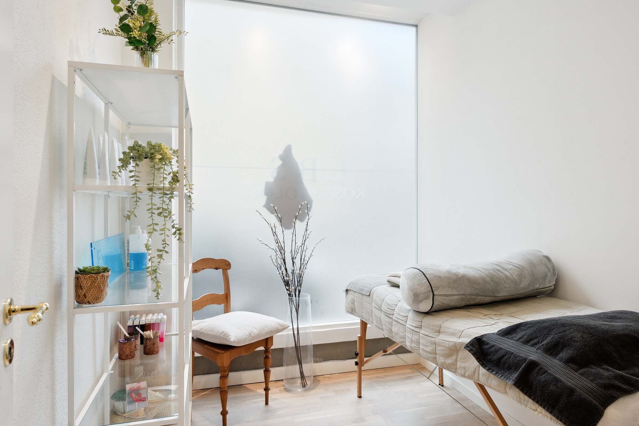 En hvid stue med en hvid væg og en trægulv med en sofa, en træstol og en hvid hylde med planter og urtikedler