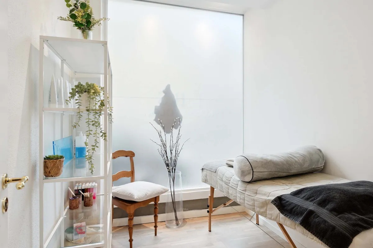 En hvid stue med en hvid væg og en trægulv med en sofa, en træstol og en hvid hylde med planter og urtikedler