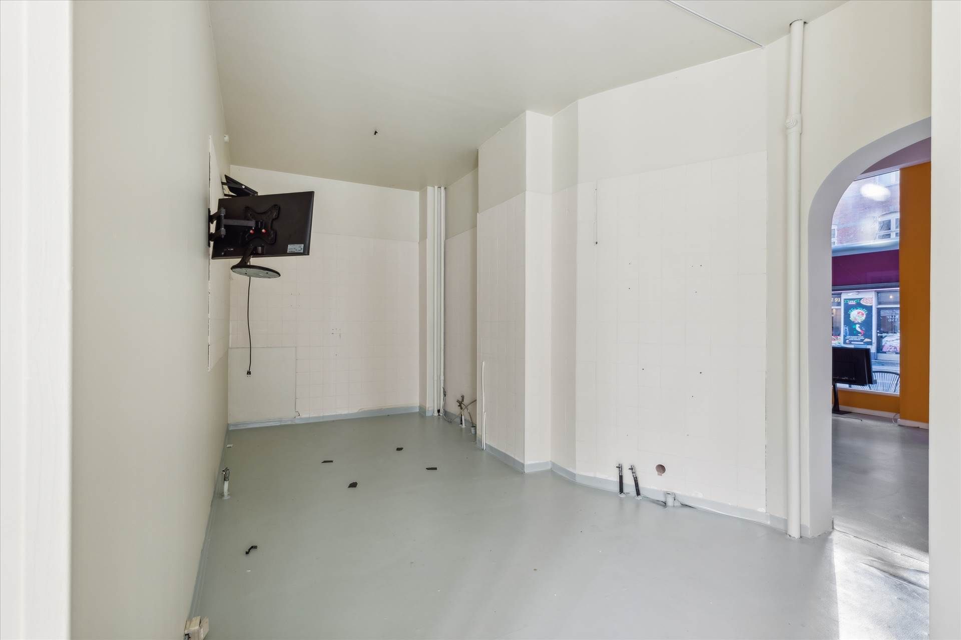 Et tomt lokale med en tv-montering på væggen og lysegule gulvbelægning