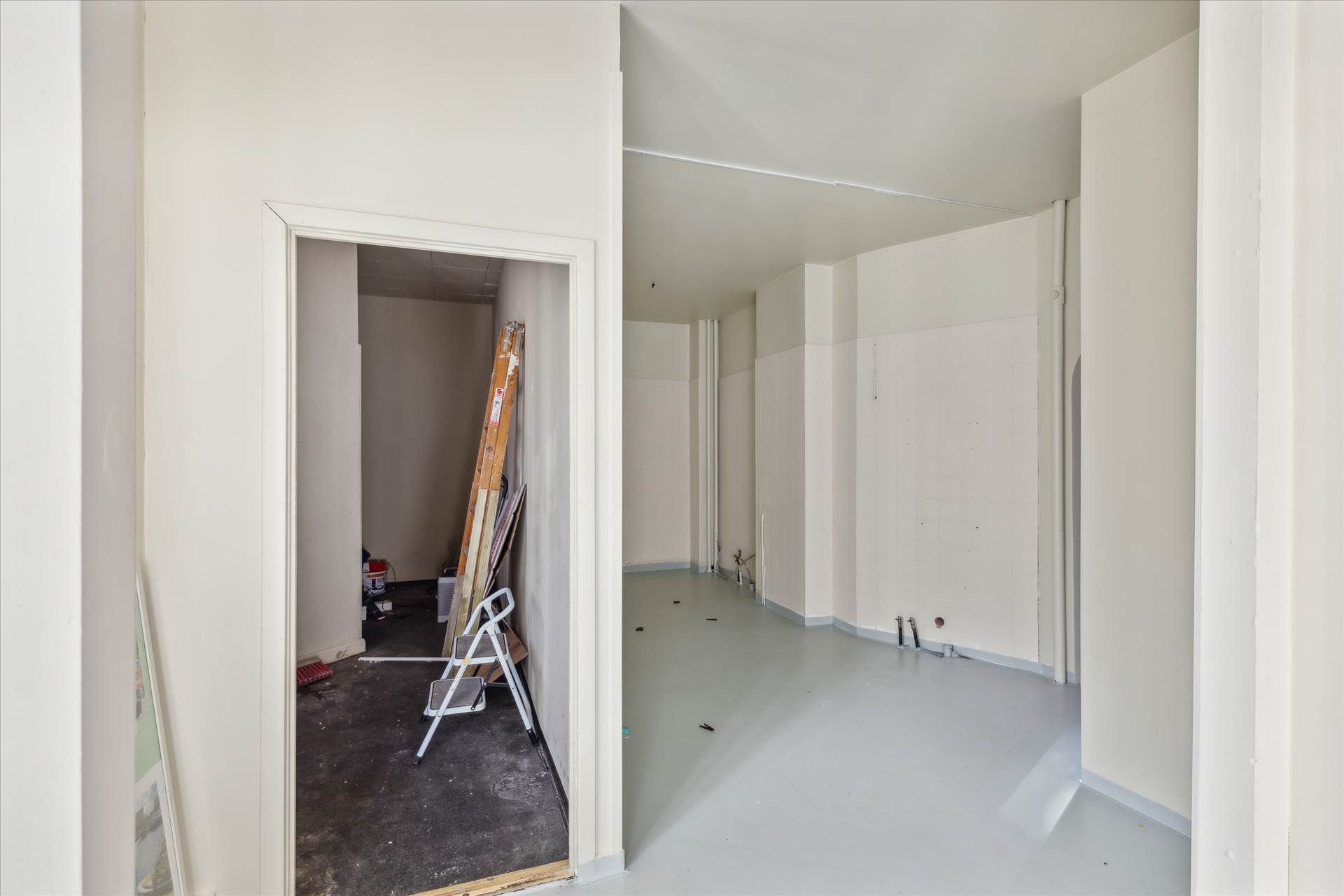 Erhvervsandel med kælder og snedækket gulv, to stige og lagermaterialer, høj hvid væg og gulv