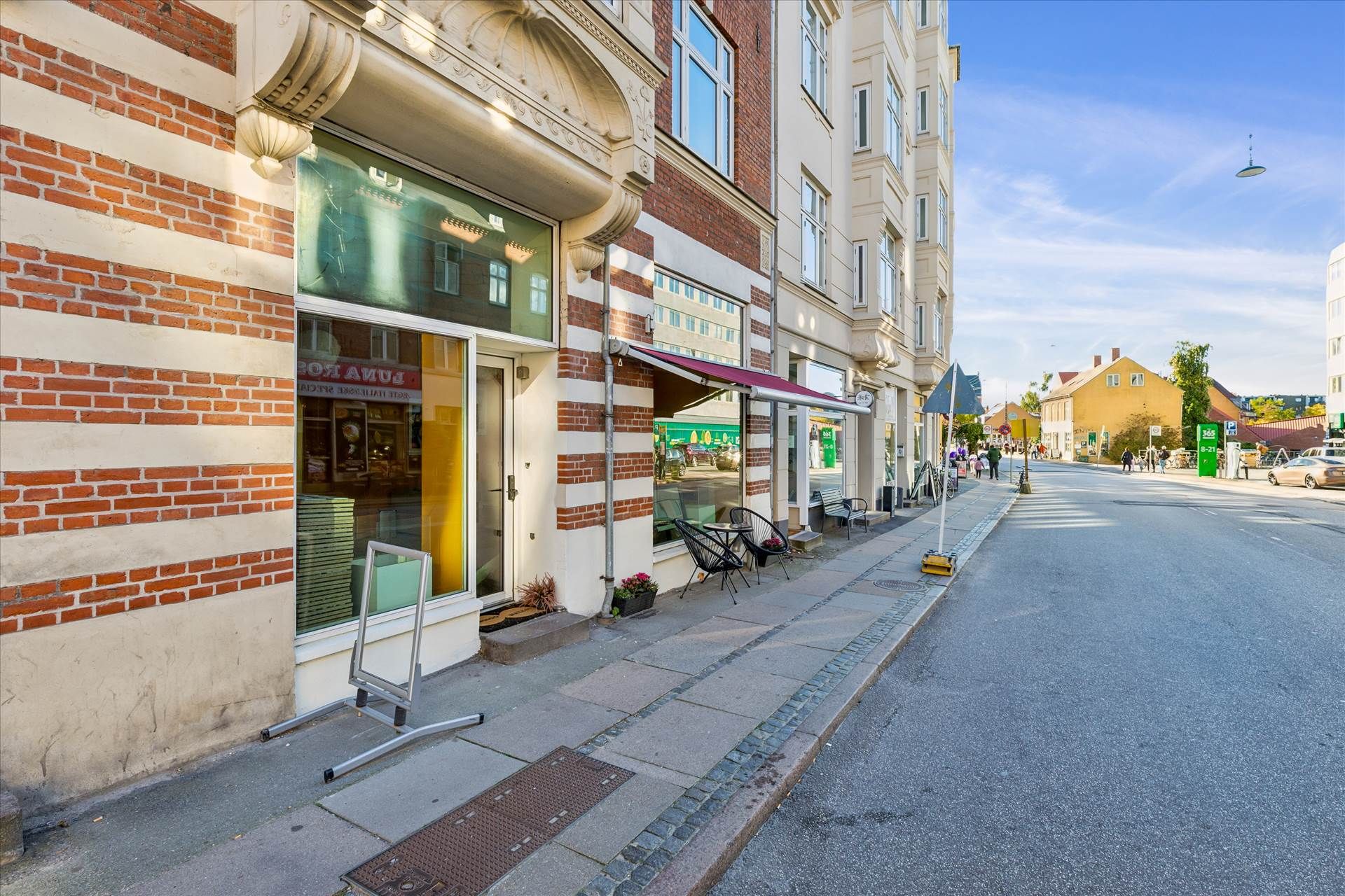 Et forretningslokal med røde og hvide mursten, glasvinduer og en rødmalet aula. Butikken med røde parasoller har udendørs