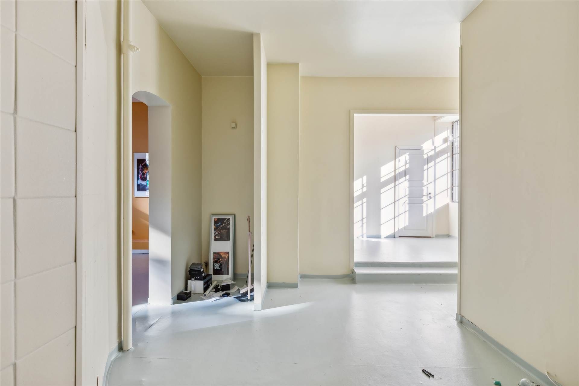 En stor, lys hall med hvide vægge og gulve samt to døre og en stige i baggrunden