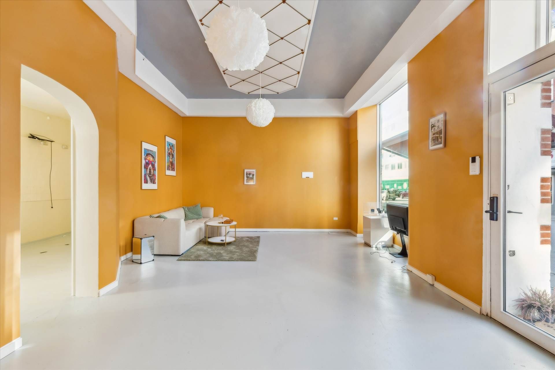 Gule vægge og hvide gulv i en stor stue med hvid sofa og to lysekroner i loftet