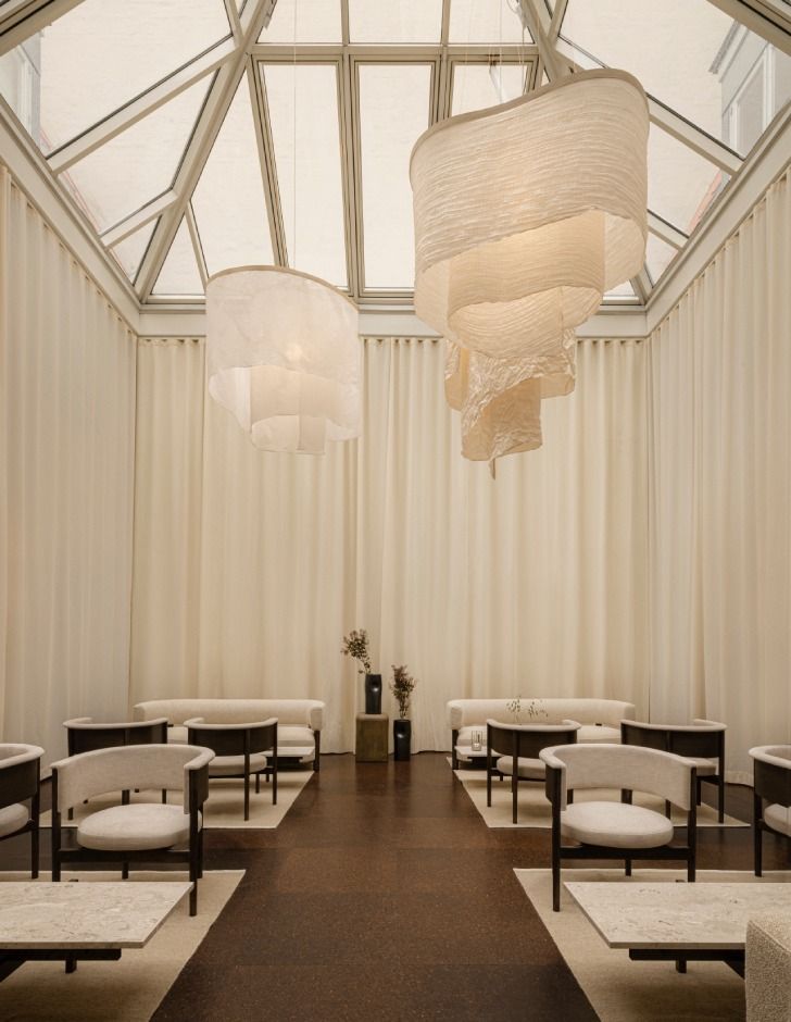 Lyse og indbydende værelse med hvide vægge og loftsvindue, to store hængelampe, hvide gardiner og møbler i lyse farver