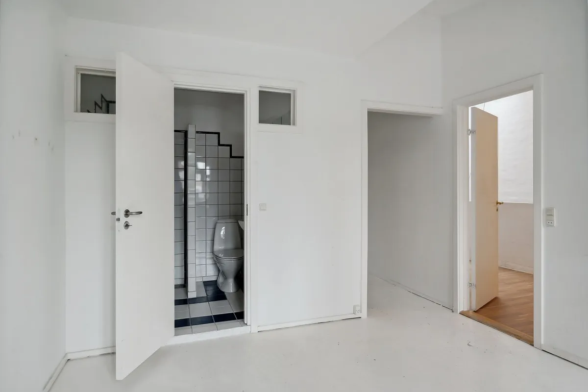 Værelse med hvid væg og højloft og toilet med hvid toiletblok og hvide kakelflader