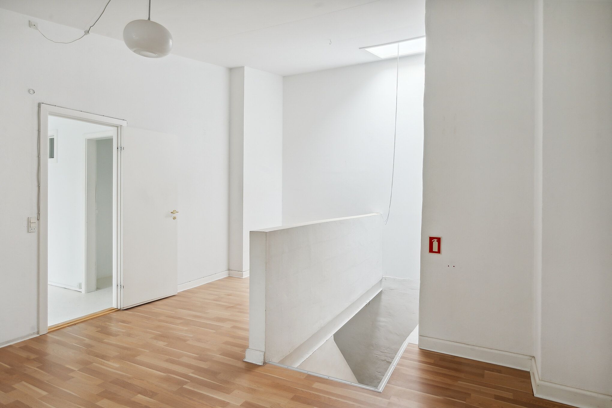 Et højloftet og lyst værksted med høj gulvdekning og åbne døre. Væggene er hvide og der er en hvid loftslampe og en