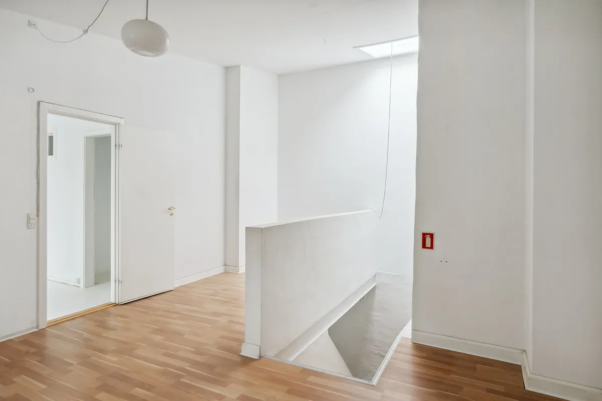 Et højloftet og lyst værksted med høj gulvdekning og åbne døre. Væggene er hvide og der er en hvid loftslampe og en