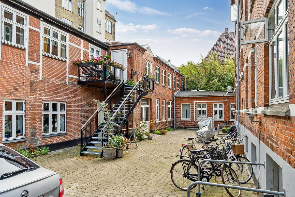 Træklægget gård med flere rækker af bygninger i røde mursten og hvide vindueskarme samt parkerede cykler og en bil