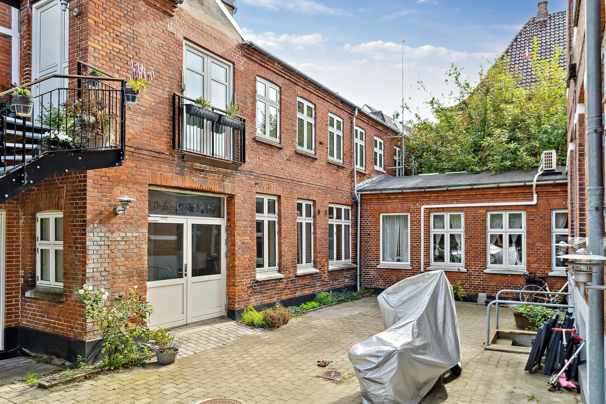 Hyggelig gård med røde murstensbygninger og lyse vinduer samt smukke haver og planter