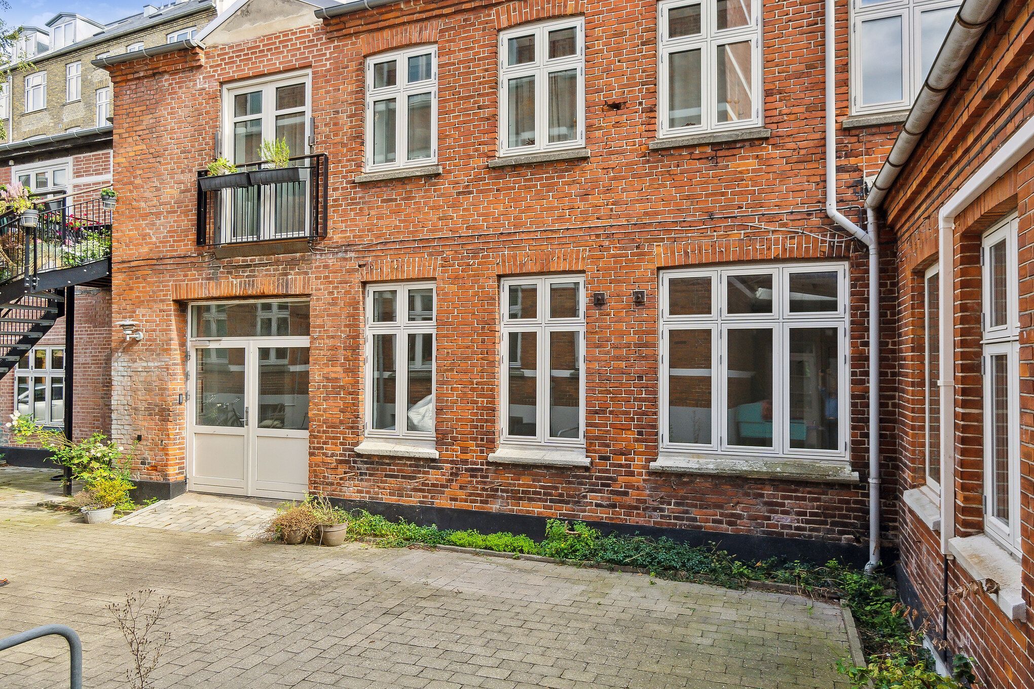 En smuk gård med røde mursten og hvide rudevindue, og en stor åben dør til værkstedet